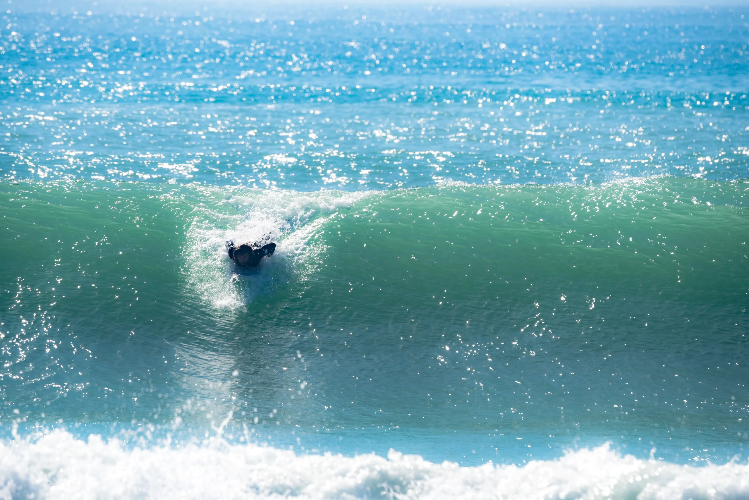 Surfeur prend une vague au Maroc, symbolisant l'expérience incluse dans le prix d'un camp surf. Soleil et mer bleue.
