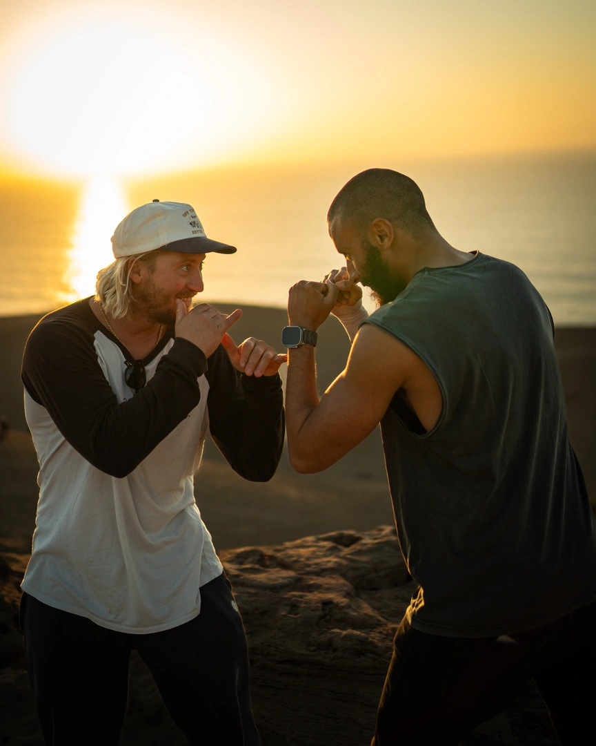 Deux hommes partageant un moment de camaraderie au coucher du soleil, parfait pour une semaine de surf.